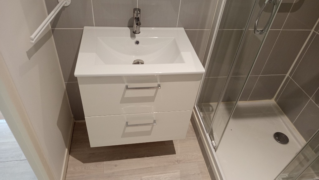 Vue rapprochée d'un meuble lavabo suspendu blanc deux tiroirs et receveur de douche posés par un plombier qualifié